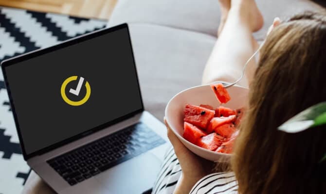 Femme mangeant des fruits rouges à côté d’un ordinateur portable ouvert